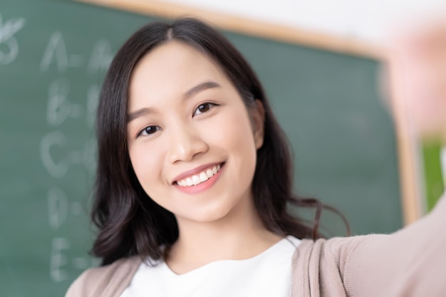 Closeup ritratto di giovane insegnante asiatico di donna attraente con un grande sorriso e prendendo selfie in classe