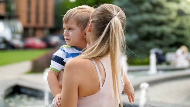 Closeup ritratto di giovane madre che abbraccia e accarezza il suo bambino piangente nel parco boy