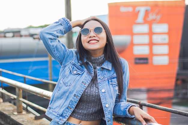 Closeup ritratto di ridere capelli lunghi ragazza in jeans giacca indossare occhiali da sole sullo sfondo della città Ragazza intelligente in piedi sul ponte Concetto di stile di vita