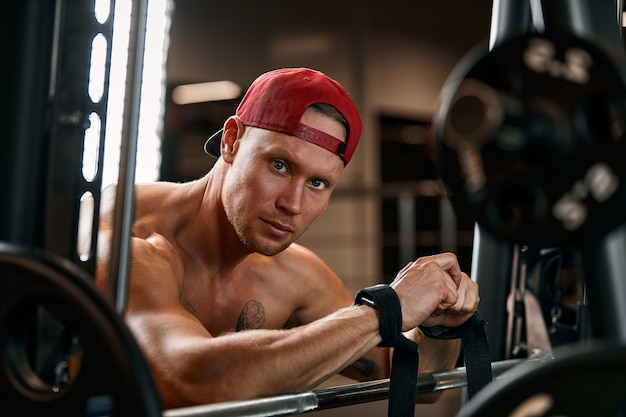 Closeup ritratto di un uomo muscoloso allenamento con bilanciere in palestra. Uomo atletico culturista brutale con six pack, addominali perfetti, spalle, bicipiti, tricipiti e petto.