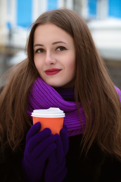 Closeup ritratto di una favolosa donna bruna che indossa una sciarpa lavorata a maglia viola e tiene in mano una tazza di caffè