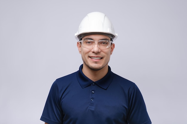 Closeup ritratto di uomo sorridente architetto costruttore in maglietta blu bianco casco e occhiali su sfondo grigio caposquadra concetto
