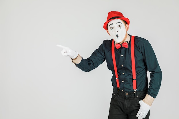 Clown con bretelle rosse e cappello rosso su sfondo bianco.