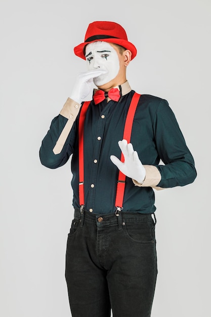 Clown con bretelle rosse e cappello rosso su sfondo bianco.