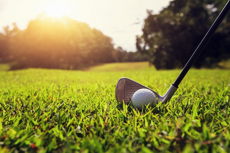 Foto club di golf del primo piano e palla da golf su erba verde con il tramonto