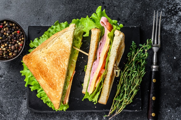 Club sandwich con prosciutto di maiale, formaggio, pomodori e lattuga su un tagliere di legno