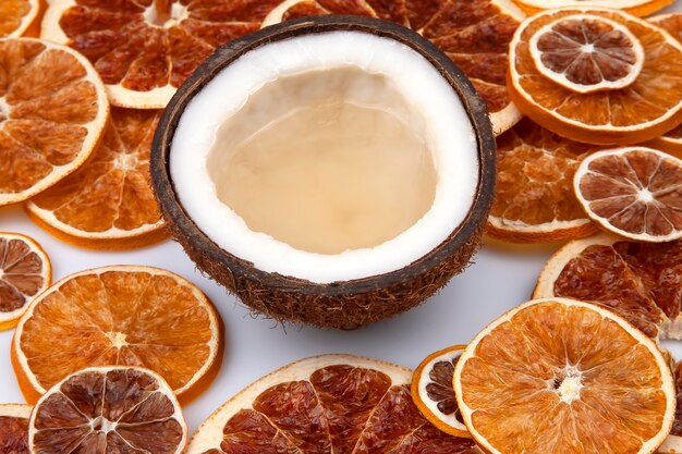 Cocco con latte naturale tra agrumi secchi su una superficie bianca