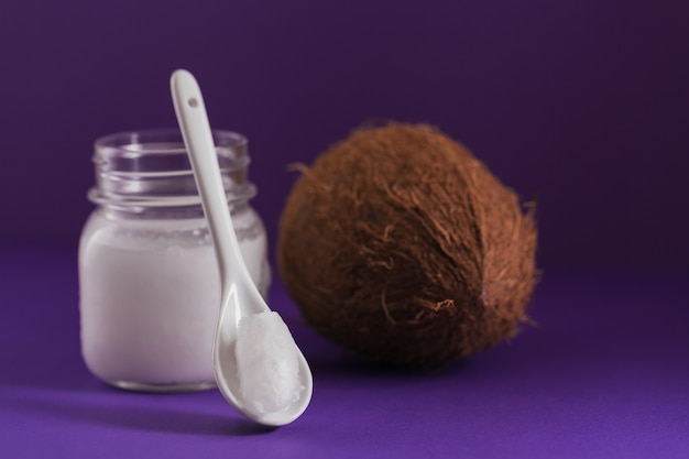 Cocco e olio di cocco in barattolo su sfondo viola. Concetto di cucina sana