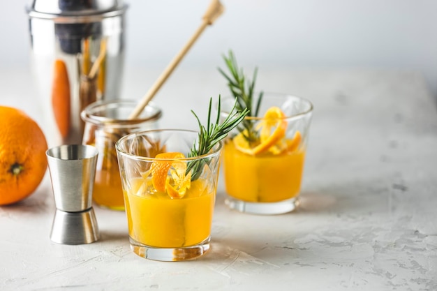 Cocktail al bourbon al miele con sciroppo semplice al rosmarino o cocktail al whisky sour fatto in casa con arancia e rosmarino Decorare la buccia d'arancia Superficie in cemento chiaro