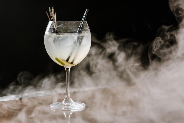 Cocktail alcolico trasparente con lime e ghiaccio sullo sfondo fumoso