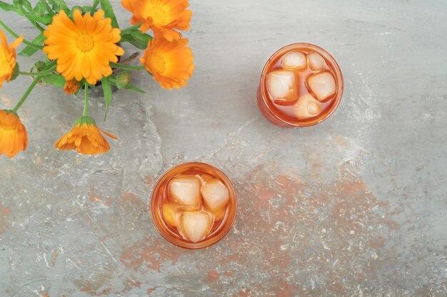 Cocktail all'arancia in bicchieri di cristallo vintage con bouquet di fiori di calendula su sfondo di pietra naturale