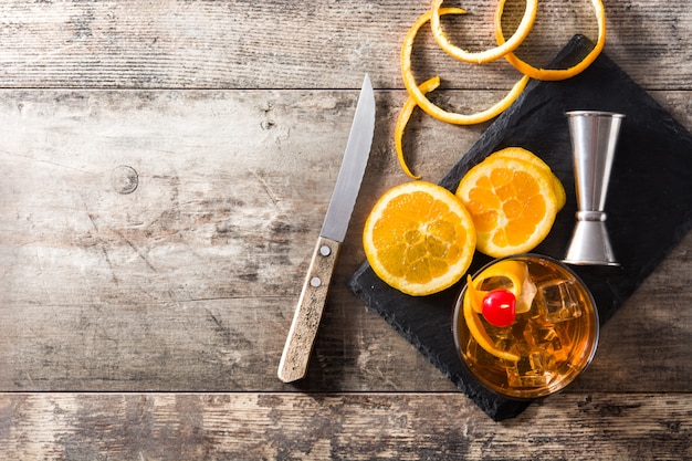 Cocktail antiquato con l'arancia e la ciliegia sulla tavola di legno, vista superiore