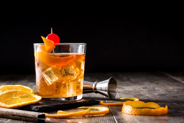 Cocktail antiquato con l'arancia e la ciliegia sulla tavola di legno