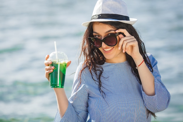 Cocktail bevente della giovane donna graziosa sulla spiaggia. Ragazza attraente che offre da bere. Limonata bevente della bella donna