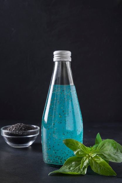 Cocktail blu di vari frutti tropicali con i semi del basilico in bottiglia. Avvicinamento. Formato verticale. Disintossicazione e freschezza.