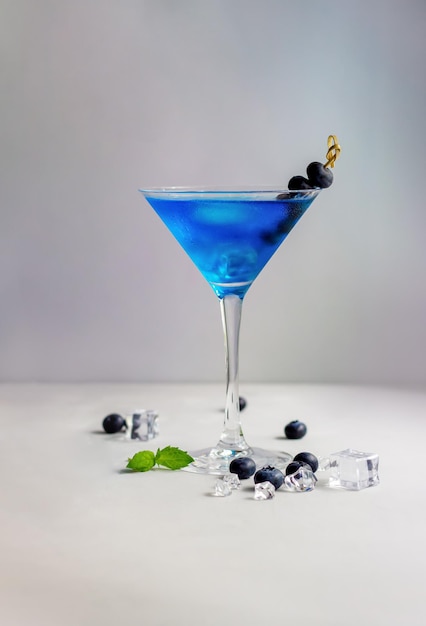 Cocktail blu in coppetta Martini con cubetti di ghiaccio menta e mirtilli