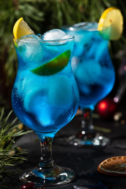 Cocktail blu in un bicchiere alto con ghiaccio e fette di limone su uno sfondo di legno