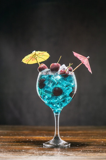 Cocktail blu in un bicchiere con ghiaccio e ciliegie