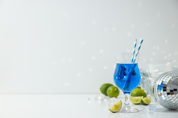 Cocktail blu in vetro lime cubetti di ghiaccio e palle discoteche su sfondo bianco spazio per il testo