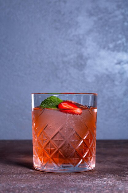cocktail con menta e fragole in un bicchiere di vetro su sfondo grigio