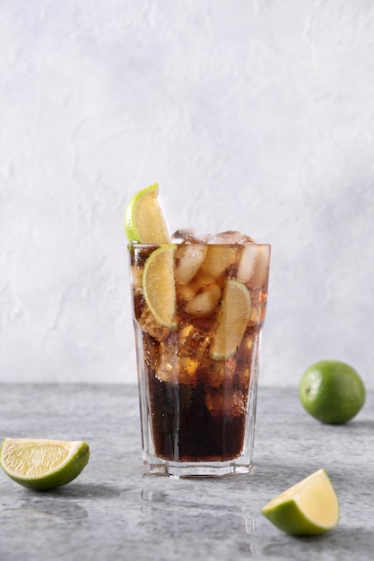 Cocktail Cuba Libre o long island ghiacciato con rom, cola, lime e ghiaccio in vetro sul tavolo di pietra grigia.