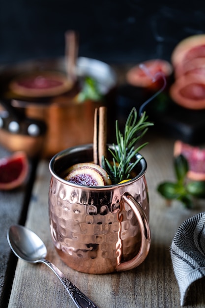 Cocktail dell'arancia sanguinella in una tazza di rame con l'arancia rossa e limone, cannella e menta su un fondo di legno. Cesto Di Vimini Arance