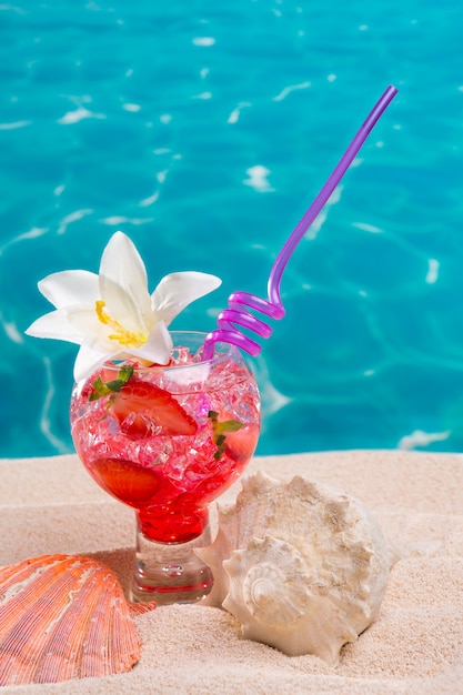 Cocktail della fragola sulla sabbia della spiaggia con i seashells