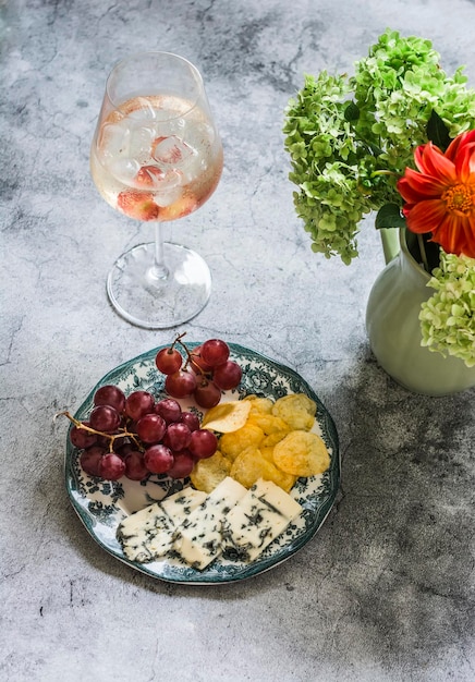 Cocktail di aperitivo e un piatto con formaggio d'uva e patatine su sfondo grigio vista dall'alto