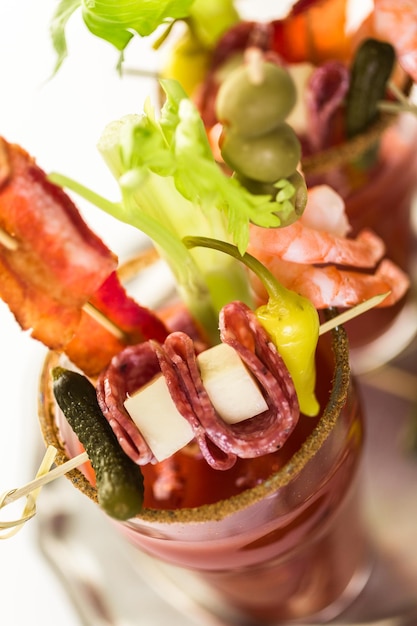 Cocktail di Bloody Mary guarnito con bastoncini di sedano, olive e striscioline di pancetta.