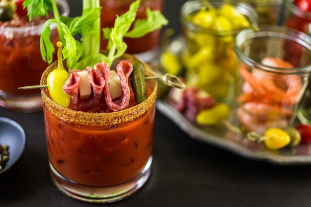 Cocktail di Bloody Mary guarnito con bastoncini di sedano, olive e striscioline di pancetta.