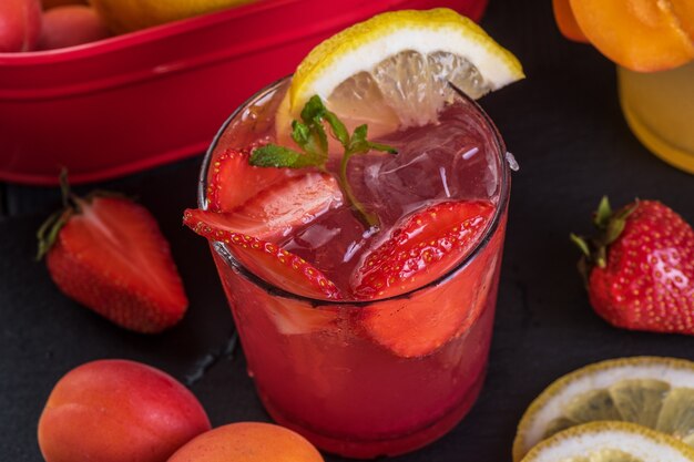 Cocktail di frutta con frutta fresca e ghiaccio. In bicchieri su fondo rustico in legno nero