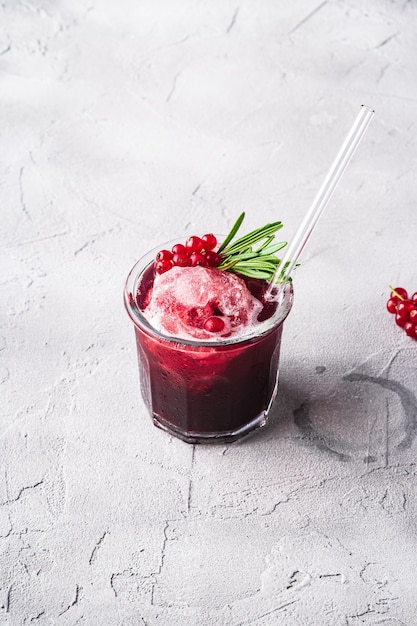 Cocktail di frutta fresca fredda in vetro, rinfrescante bevanda estiva a bacca di ribes rosso con foglie di rosmarino