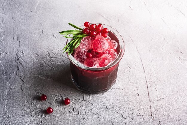 Cocktail di frutta ghiacciata fresca in vetro, rinfrescante bevanda estiva a bacca di ribes rosso con foglia di rosmarino