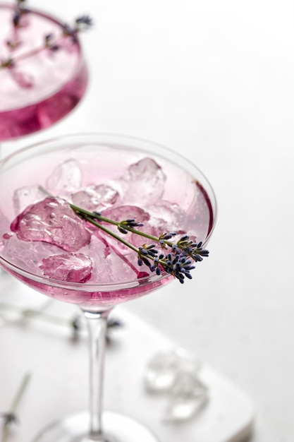 Cocktail di lavanda Bevanda viola in un bicchiere su bordo bianco e sfondo bianco con ghiaccio e lavanda