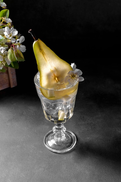 Cocktail di pere in un bicchiere decorato con frutta fresca e fiori su sfondo grigio scuro