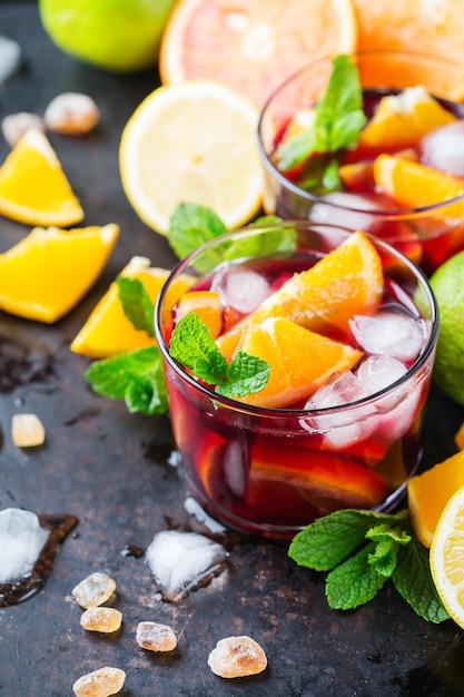 Cocktail di sangria spagnola fredda tradizionale con vino rosso e ingredienti su un tavolo nero agrumi arancia lime limone foglie di menta e ghiaccio per le calde giornate estive