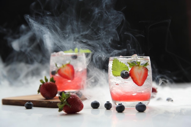 Cocktail di succo di fragola con ghiaccio e menta su sfondo nero e fumo