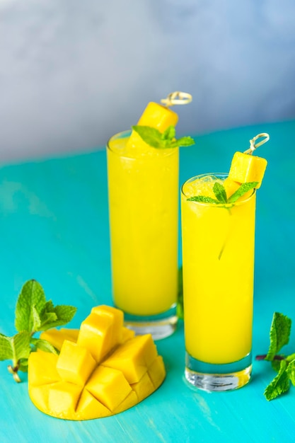 Cocktail estivi rinfrescanti a base di bevanda fredda al mango o una bevanda con ghiaccio su sfondo grigio blu Cocktail o succo di mango ghiacciato fresco estivo con menta e frutta di mango