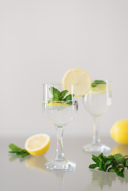 Cocktail fatto in casa con acqua minerale frizzante a fette di limone e foglie di menta fresca su un tavolo di vetro