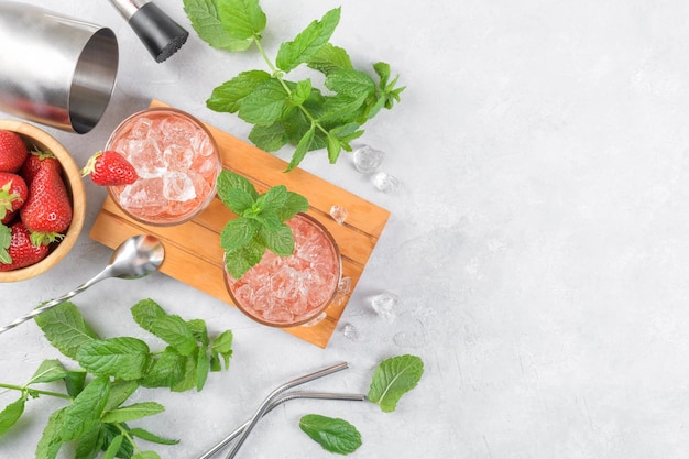 Cocktail freddo alla fragola mojito margarita daiquiri in due bicchieri con ghiaccio alla menta e strumenti da barista sul tavolo luminoso