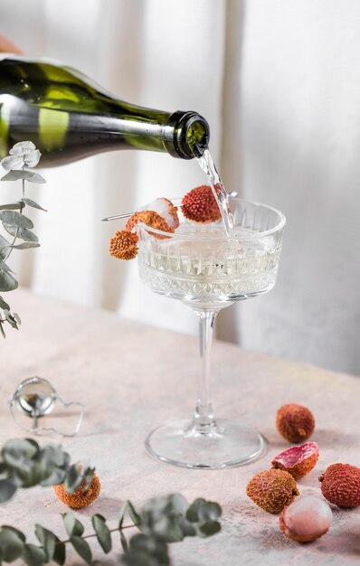 Cocktail freddo di litchi appena spremuto con champagne e frutta fresca su uno sfondo di cemento grigio chiaro Spazio per la copia di messa a fuoco selettiva