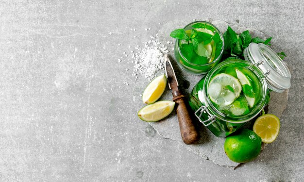 Cocktail in barattolo - foglie di menta, ghiaccio, rum e lime su una base di pietra con un coltello per agrumi e zucchero.