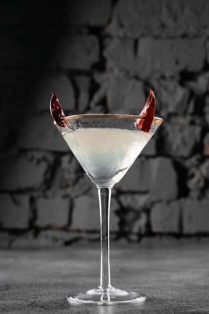 Cocktail in vetro con peperoncino rosso sulla superficie grigia. Bevanda alcolica del diavolo.