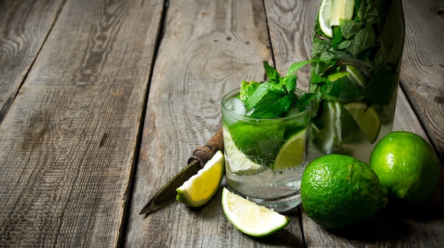 Cocktail in vetro e bottiglia, anche menta e lime su un tavolo di legno. Spazio libero per il testo.