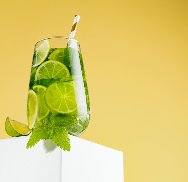 Cocktail Mojito sul podio con un tubo di carta, uno spicchio di menta e lime, sfondo giallo sfumato. Uno dei set mojito