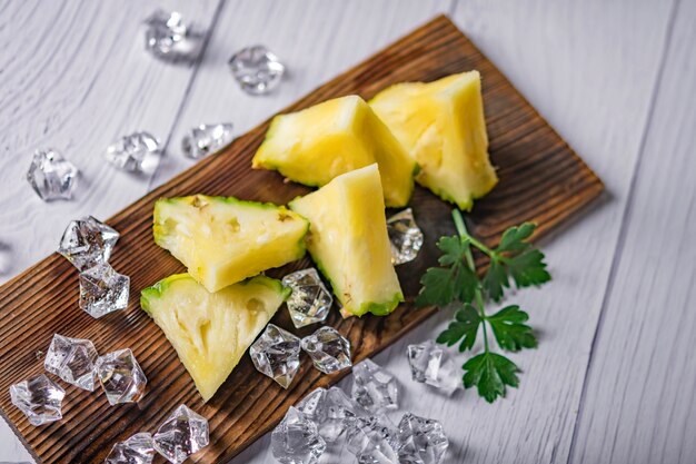 Cocktail o succo di ananas con ghiaccio e ananas su uno sfondo scuro