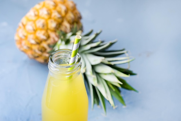 Cocktail o succo di ananas gustoso in bottiglia di vetro con paglia e ananas su sfondo blu