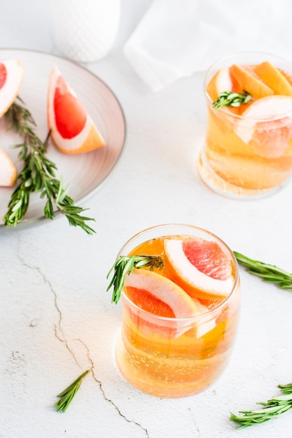 Cocktail rinfrescante al pompelmo con rosmarino in bicchieri e frutta su un piatto sul tavolo Bevanda fatta in casa Vista verticale