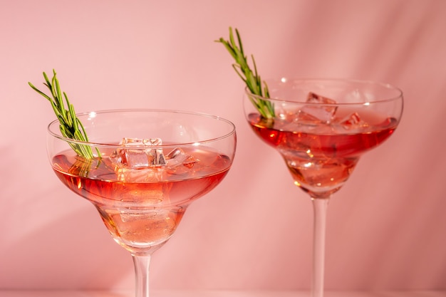 Cocktail rinfrescante con rosmarino in un bicchiere su una parete luminosa.