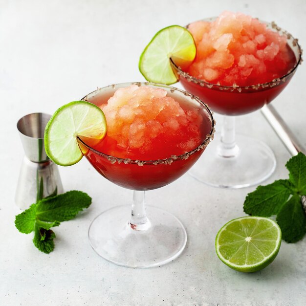 Cocktail rinfrescante Red Frozen Margarita sul tavolo e lime con menta